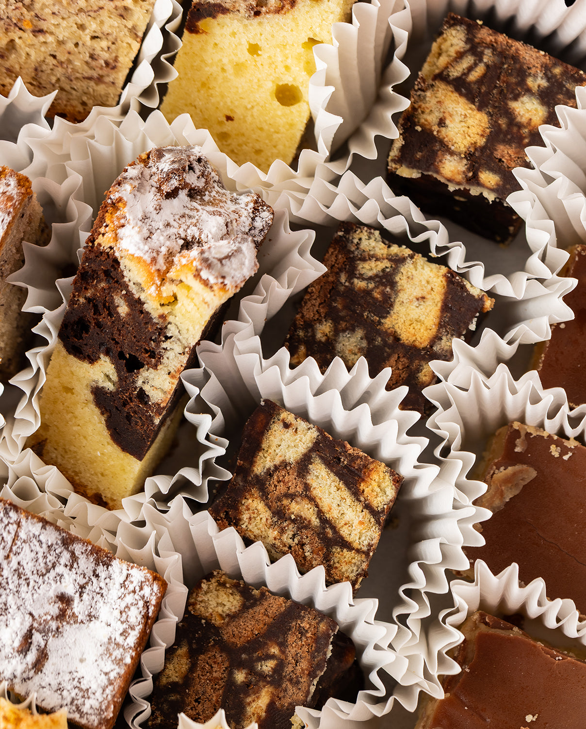 Assorted selection of cakes in white paper cups 