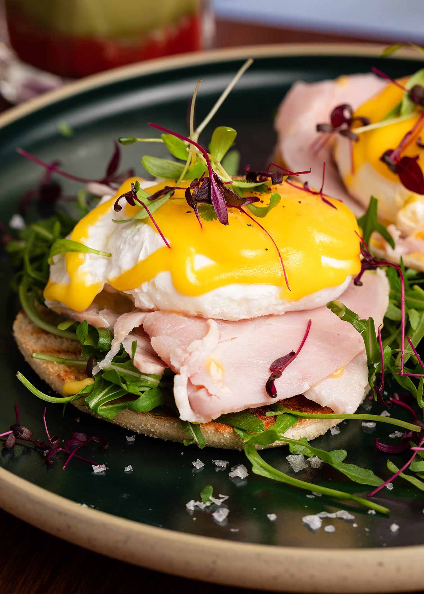 Close-up of a sandwich with poached eggs, ham, and salad on a plate.