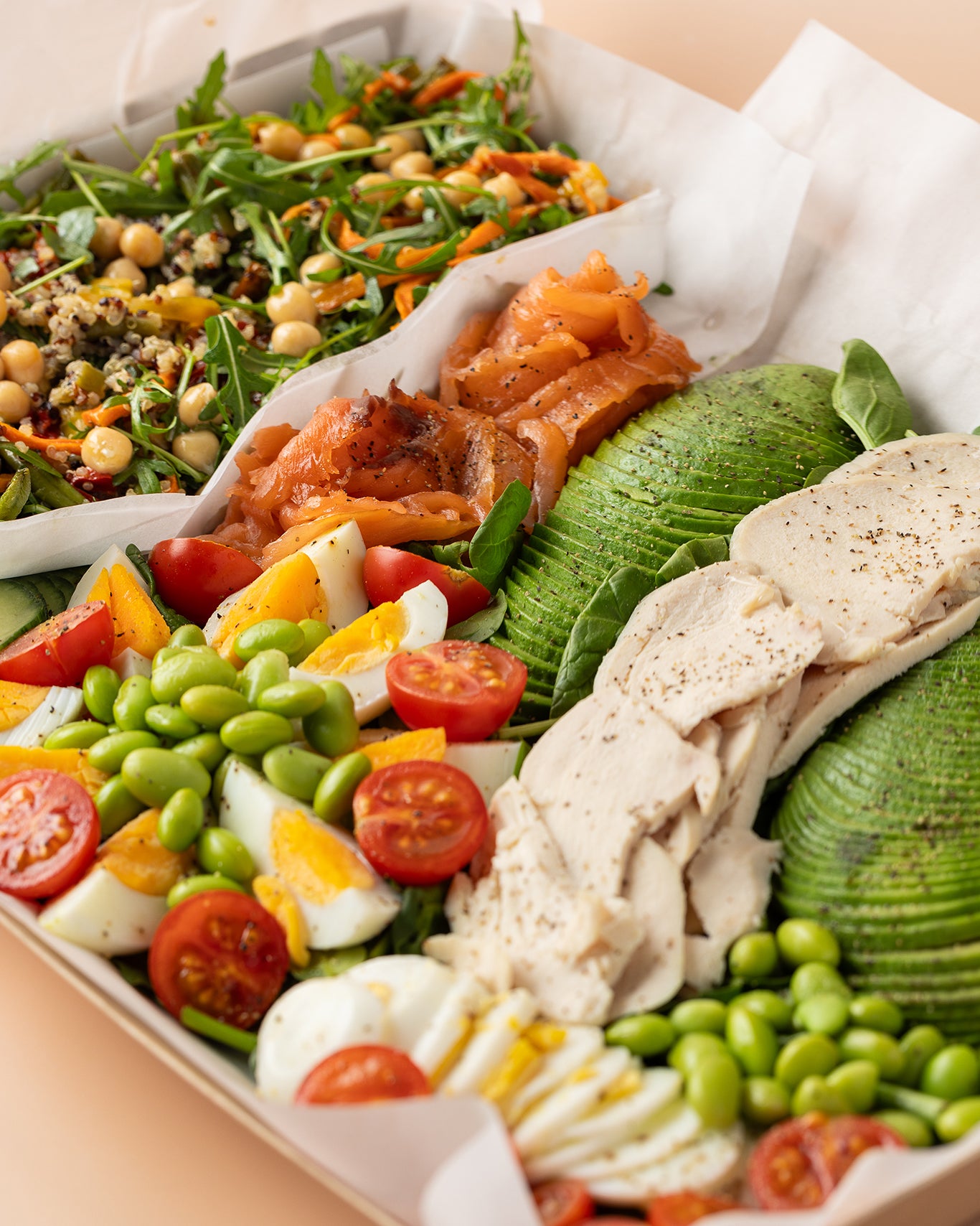 Assorted salad with chicken, avocado, tomatoes, and other vegetables in a box.