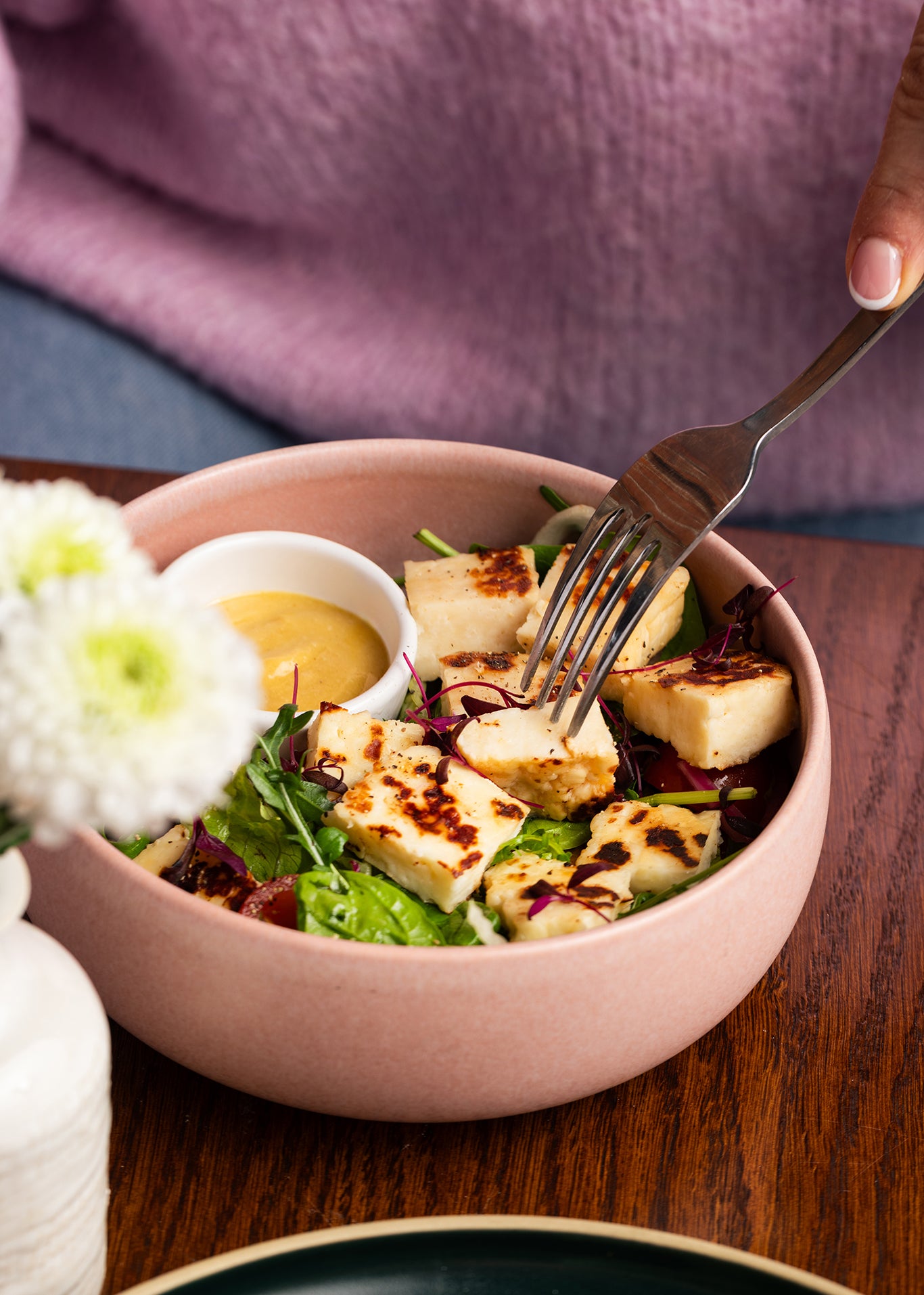 Bowl of salad with grilled haloumi on a wooden table.